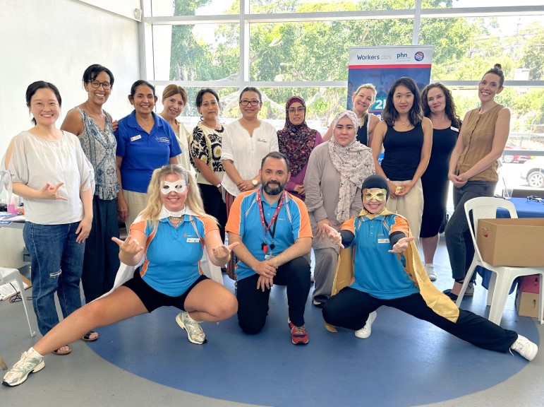 Group of adults posing at a diabetes screening event, with two staff in superhero-style outfits at the front.